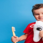 Niño feliz con cepillo de dientes y un peluche de un diente