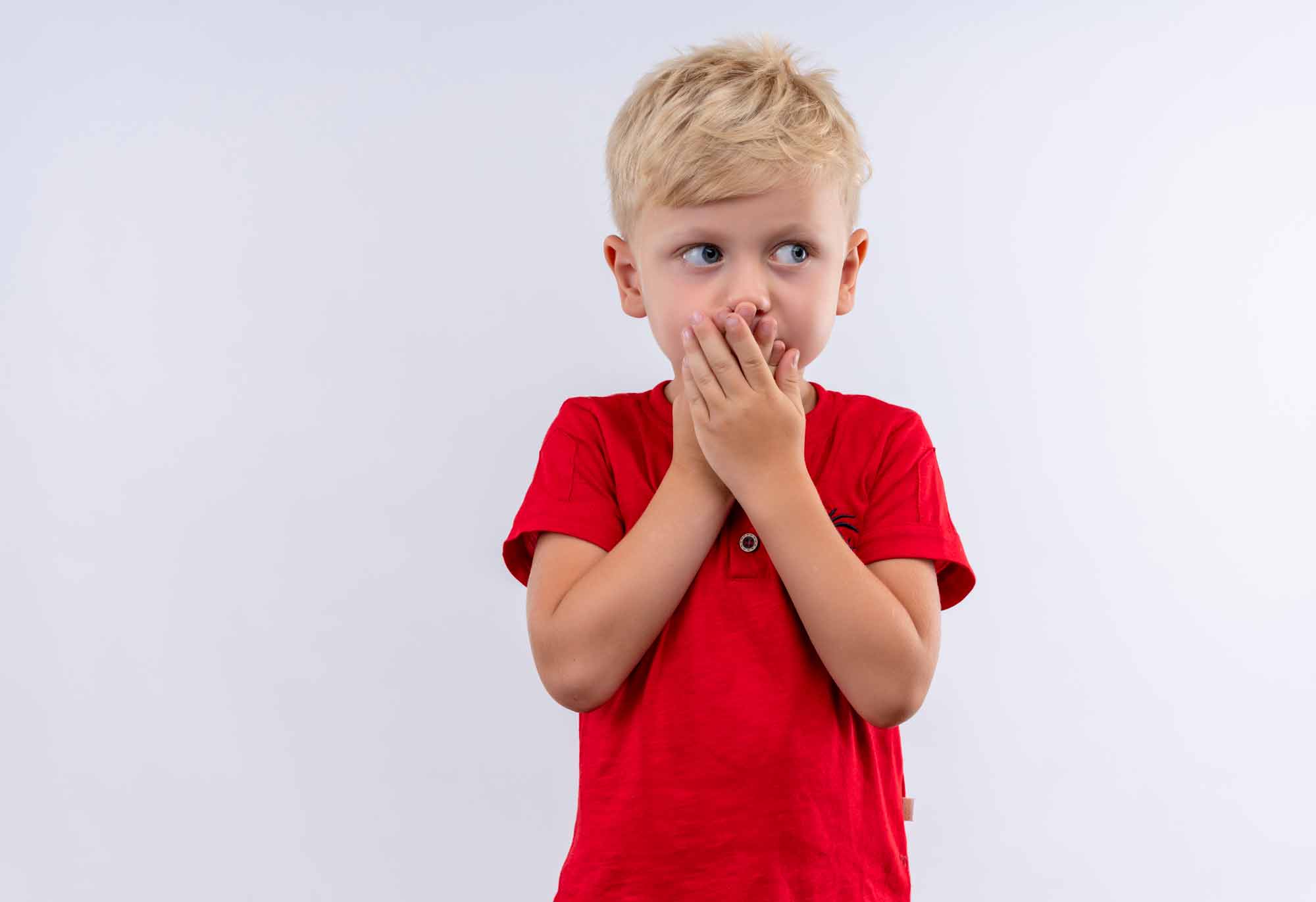 Niño tapandose la boca con camiseta roja sobre fondo blanco