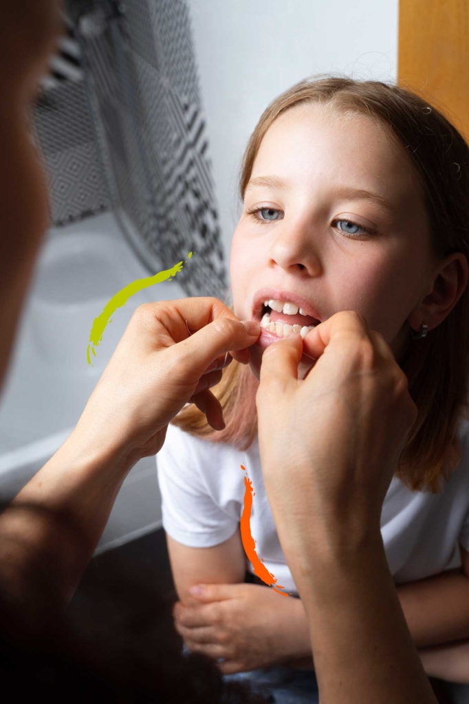 persona limpiando dientes de una niña con hilo dental