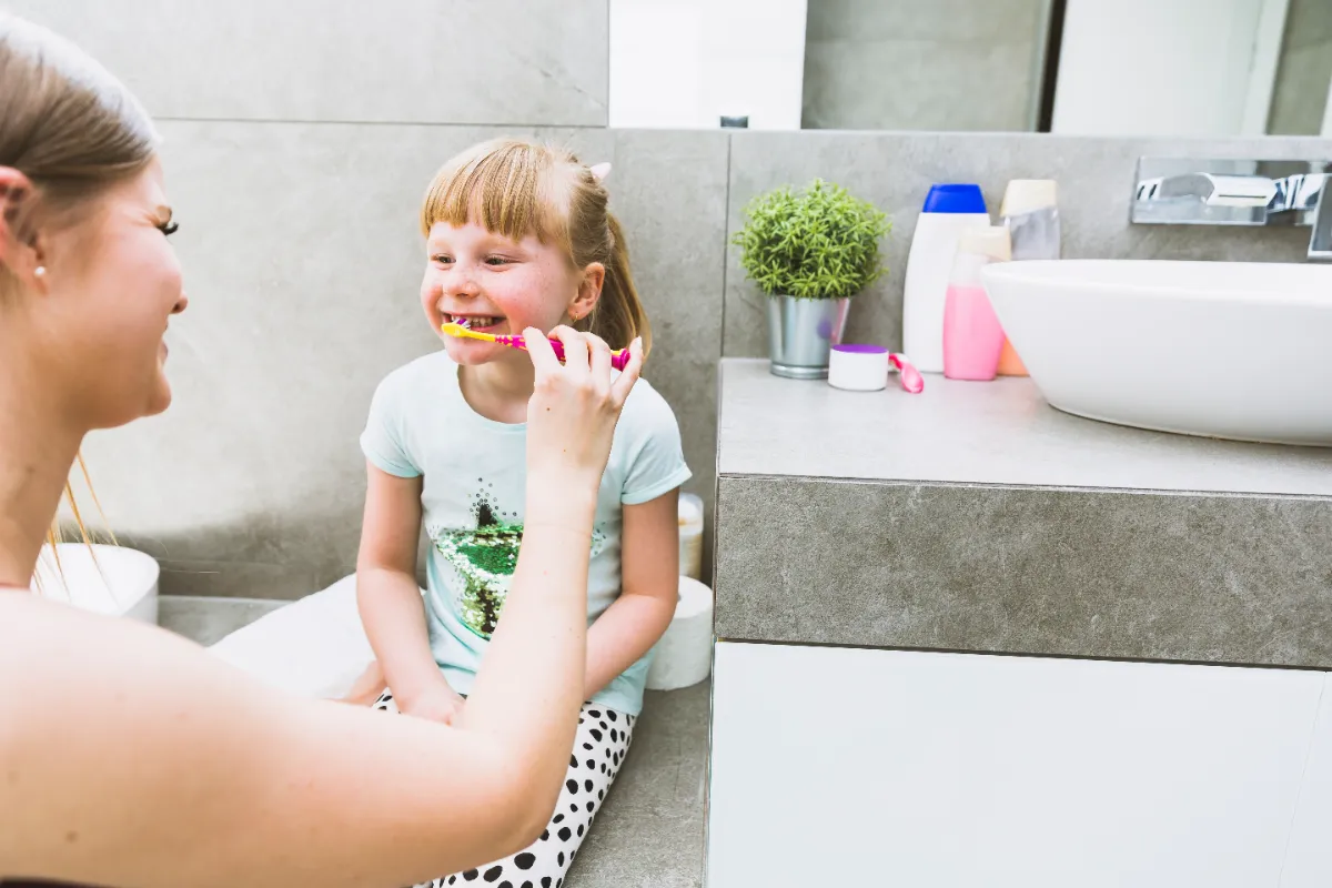 Madre cepillando los dientes a su hija con pasta fluorada tras el jarabe antibiótico