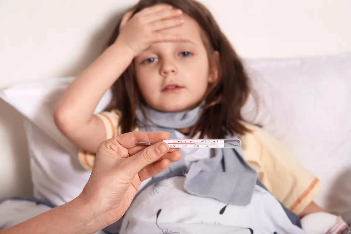 Niña con fiebre en la cama mientras su madre mira el termómetro